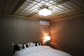A hotel room with a bed, a wall-mounted air conditioner, and a ceiling light fixture.