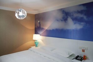 A hotel room with a bed, a globe light, a wall mural, a nightstand with a lamp, and a phone on the nightstand.