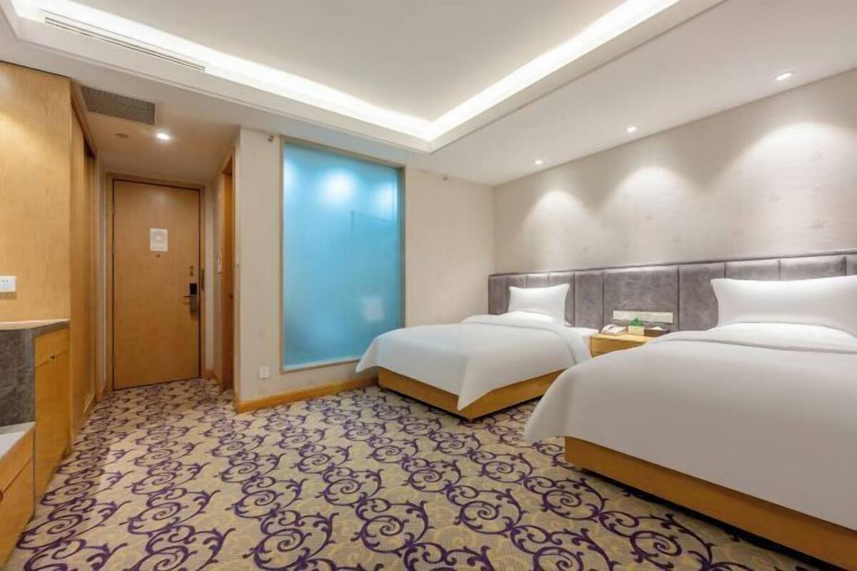 Une chambre d’hôtel avec deux lits, une moquette à motifs, une porte en bois et un mur bleu.