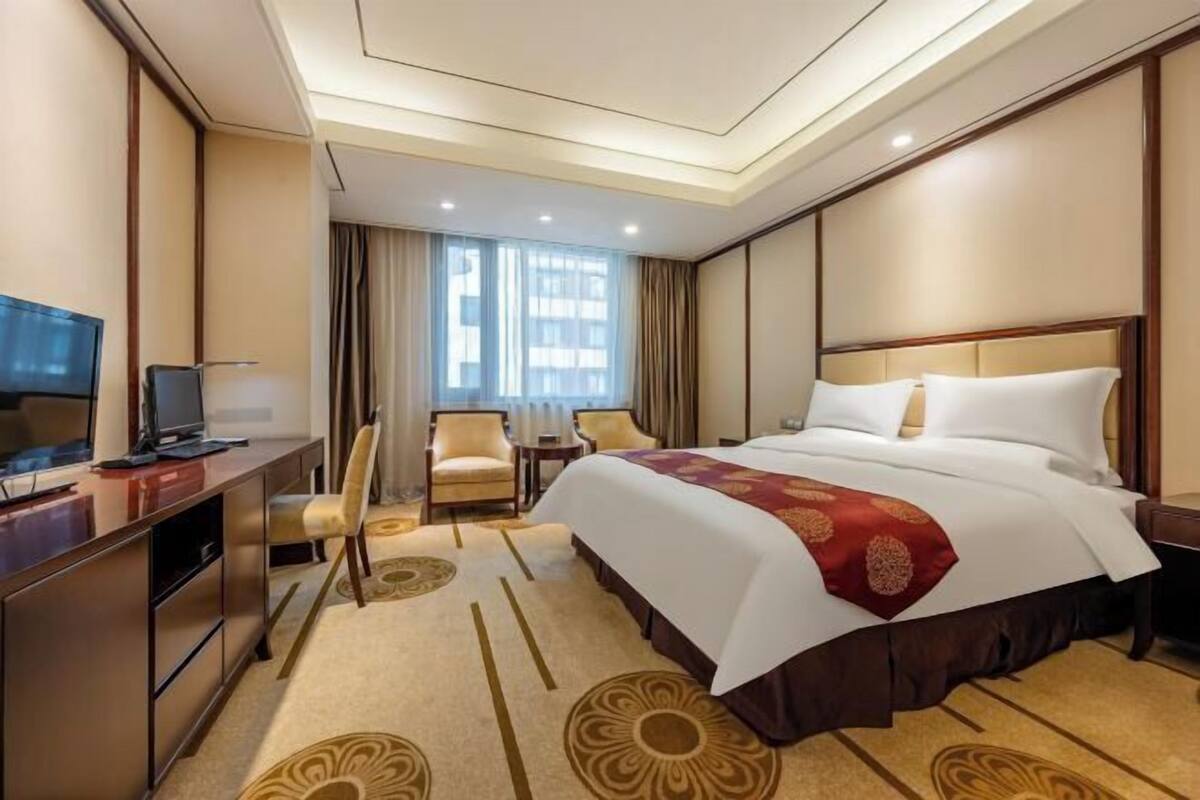 Une chambre d’hôtel avec un lit, un bureau avec une télévision, une chaise et une fenêtre avec des rideaux.