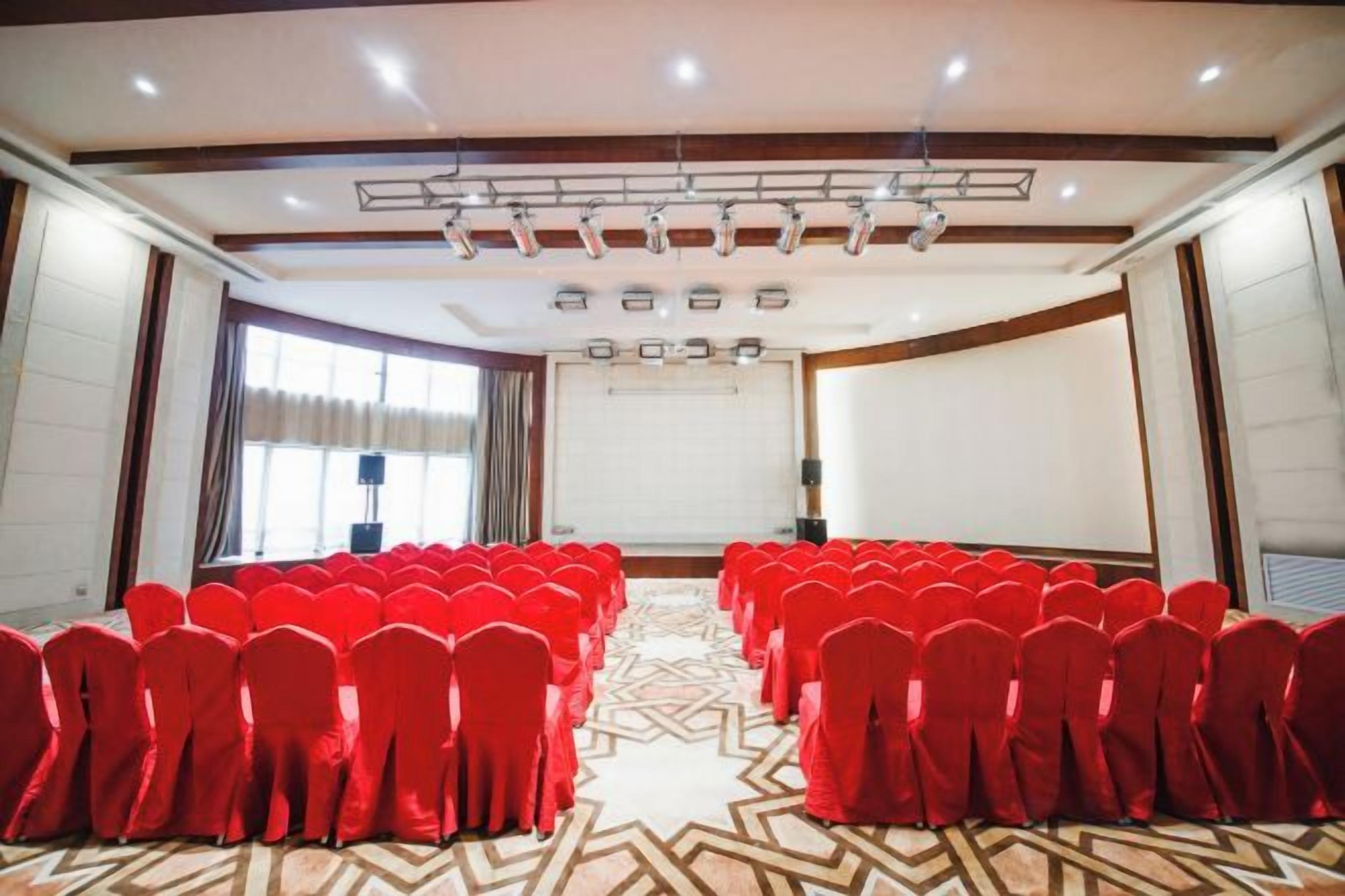 Une salle de conférence avec des rangées de chaises, un écran de projection et une grande fenêtre.