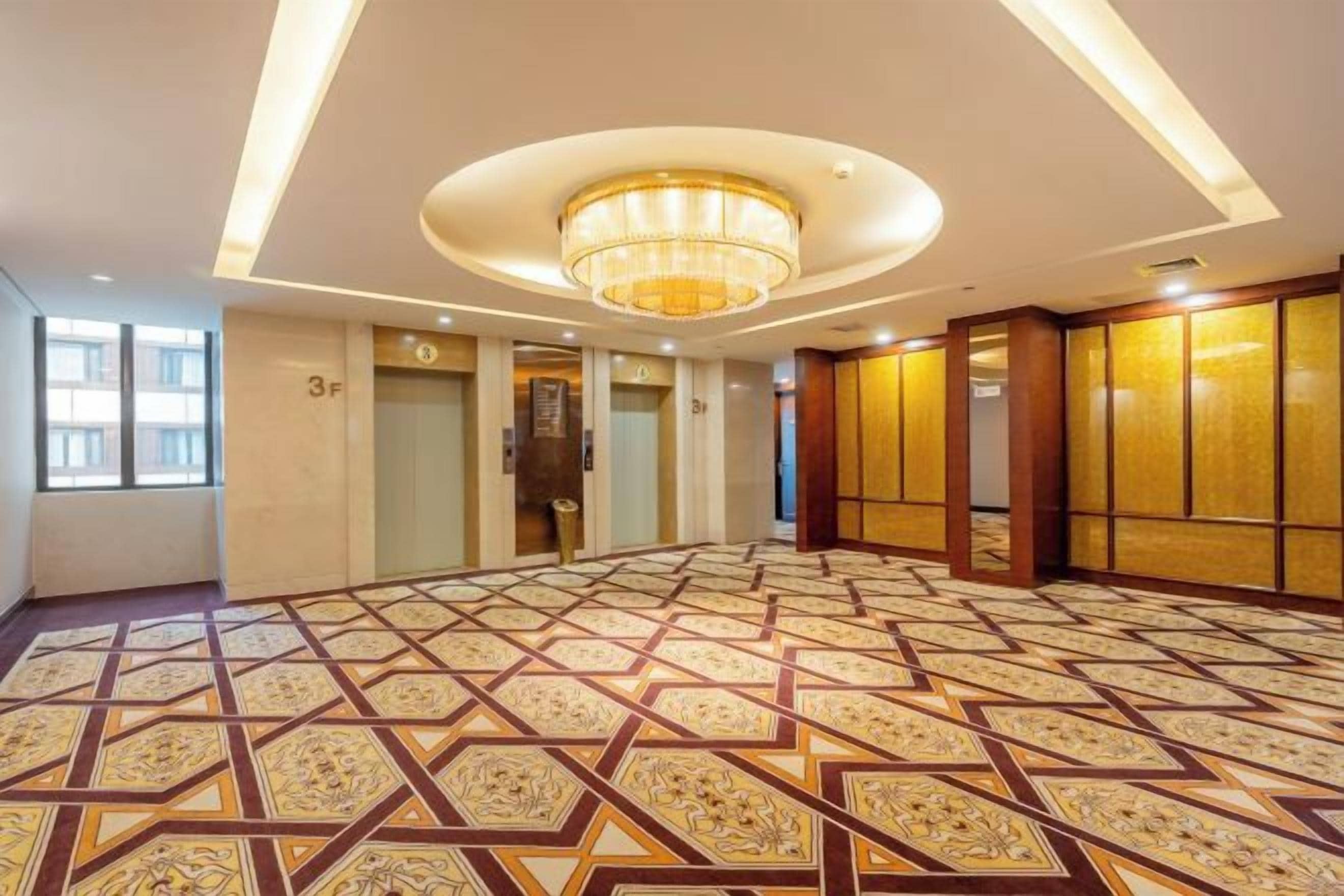A spacious hotel lobby with a patterned floor, a chandelier, and a view of the exterior through large windows.
