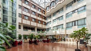 Monikerroksisen hotellin aula, jossa on lasikatto, useita kerroksia ja sisätiloissa olevia kasveja.