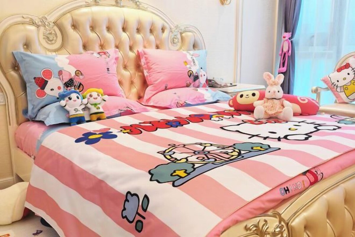 A bed with a Hello Kitty-themed bedspread, plush toys, and a tufted headboard.