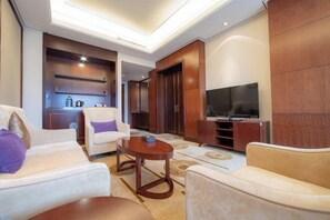 A modern living room with a sofa, armchair, and a coffee table. There is a television and a wooden cabinet. - Chang'an Baiyun Hotel (Beijing)