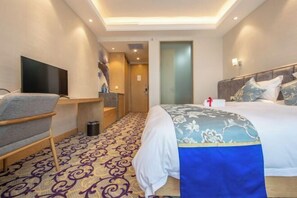 Ein modernes Hotelzimmer mit einem großen Bett, einem Flachbildfernseher, einem Schreibtisch und einem gemusterten Teppich.