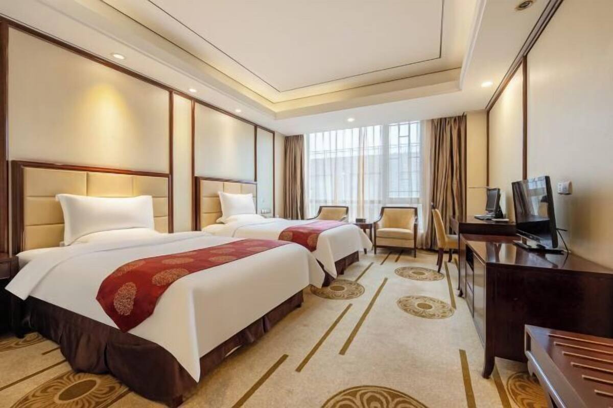 Une chambre d’hôtel avec deux lits, un bureau, une télévision et une fenêtre avec des rideaux.