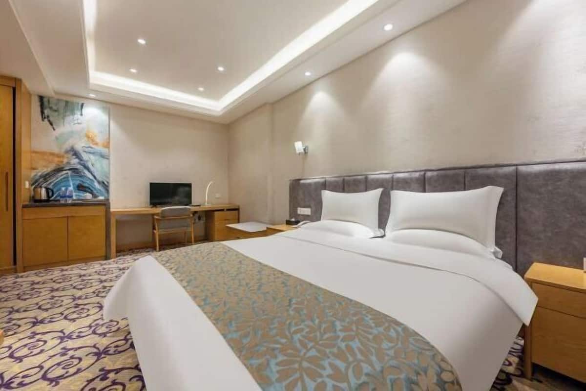 Une chambre d’hôtel avec un grand lit, un bureau avec une chaise, une télévision et un tableau au mur.