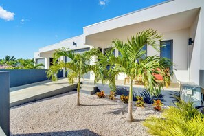 Un edificio moderno con techo plano, un espacio al aire libre cubierto con palmeras y suelo de grava.