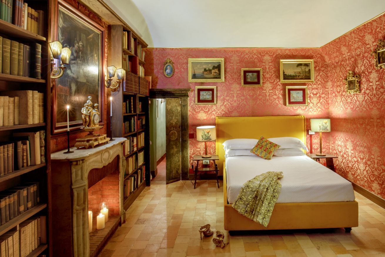 A bedroom with a large bed, a fireplace, bookshelves, and framed pictures on the walls.