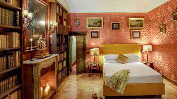 A bedroom with a large bed, a fireplace, bookshelves, and framed pictures on the walls.