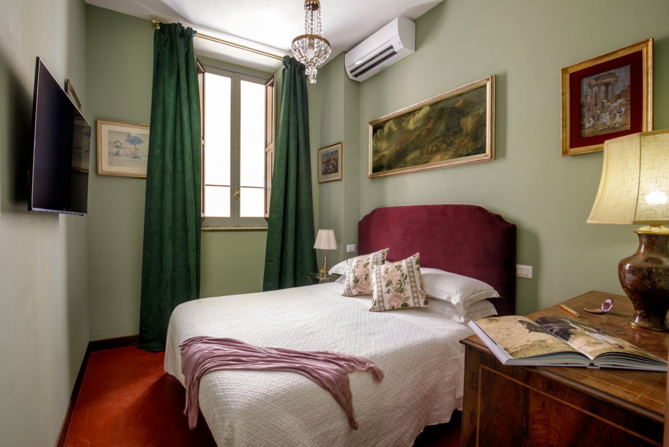 Een hotelkamer met een bed, een flatscreen televisie, een bureau met een lamp en een raam met gordijnen.