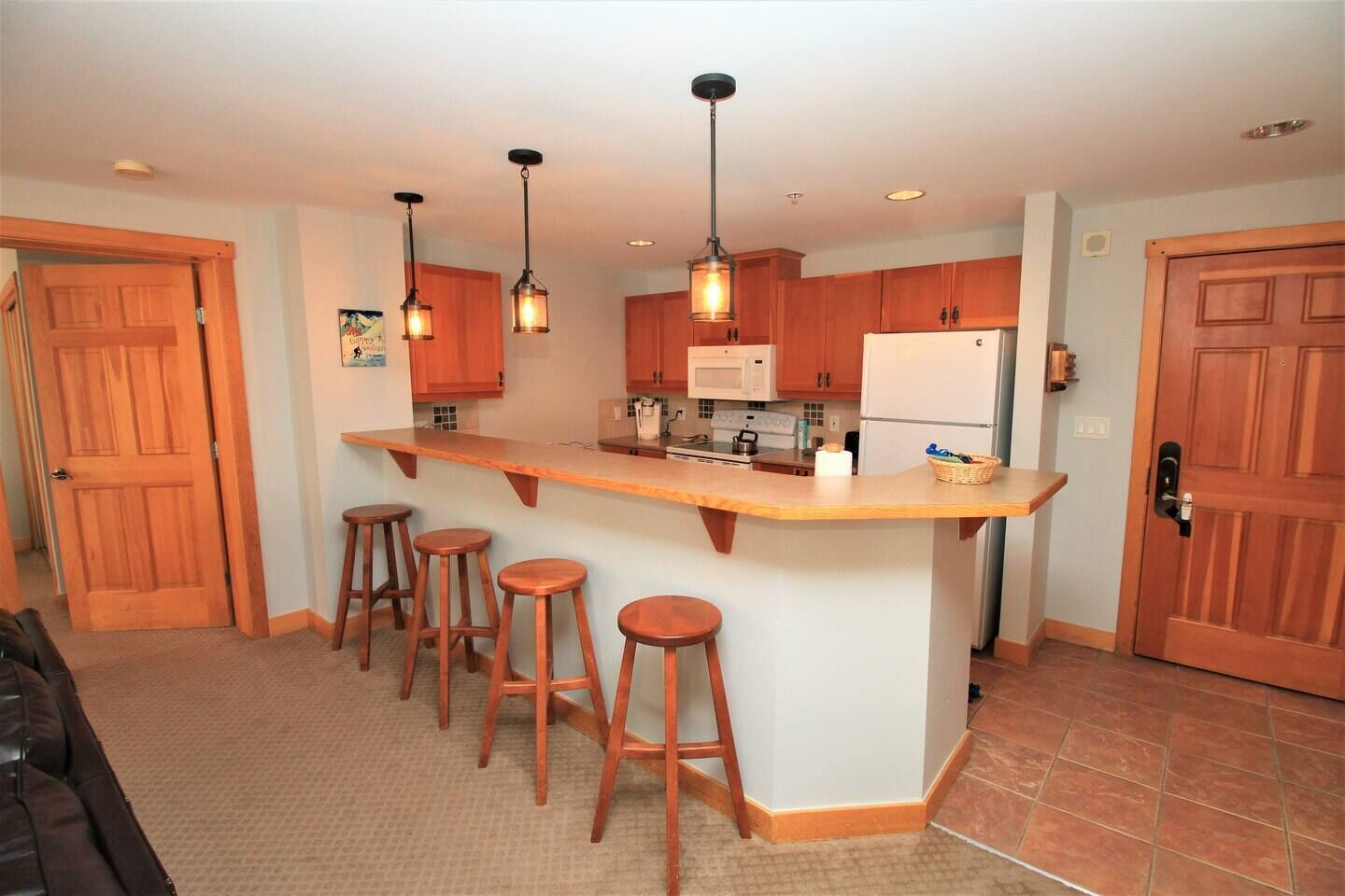 Une cuisine avec des meubles de rangement en bois, un îlot central doté de tabourets, des luminaires suspendus et un réfrigérateur.