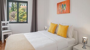 Ein Schlafzimmer mit einem Bett, zwei Nachttischen, einem Sessel, einem Fenster mit Vorhängen und einem Bild an der Wand.