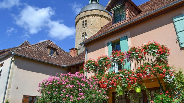 Un edificio histórico con una torre, un balcón lleno de flores y un cielo azul despejado.