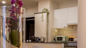 A modern kitchen with white cabinets, a microwave, and a stove. There is a glass table with candles and a vase of flowers. - Morgana Charming Apartment Close to Vatican (ROMA)