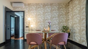 A modern dining area with a glass table and two pink chairs, a patterned wallpaper, and a potted plant. - Morgana Charming Apartment Close to Vatican (ROMA)