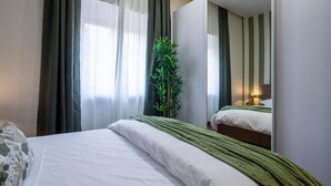 A neatly made bed with white linens and a green throw blanket, a potted plant, and a mirror reflecting the room. - Morgana Charming Apartment Close to Vatican (ROMA)