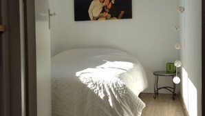 Un dormitorio con cama, un cuadro en la pared, una mesita y una ventana.