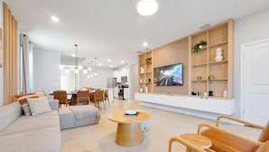Ein modernes Wohnzimmer mit einer Couch, einem Couchtisch und Holzstühlen. Es gibt eine Essecke mit Stühlen und einem Tisch, und im Hintergrund eine Küche.