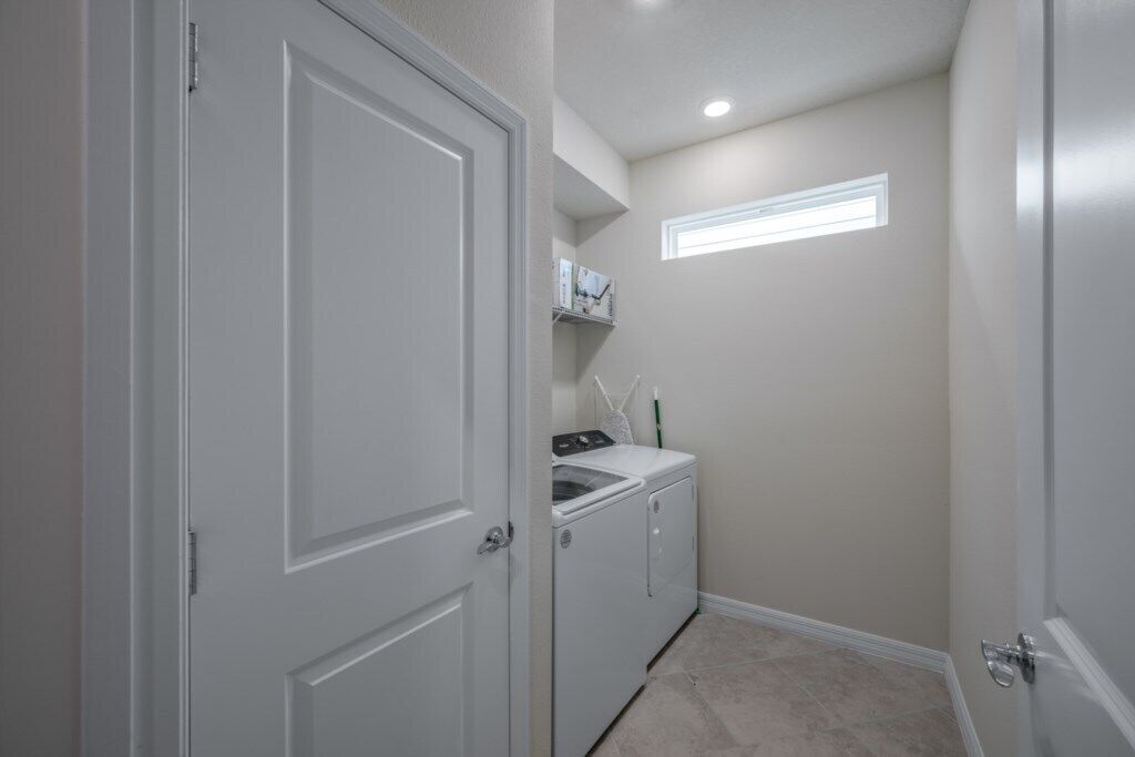 A laundry room with a washing machine and dryer, a small window, and a door.