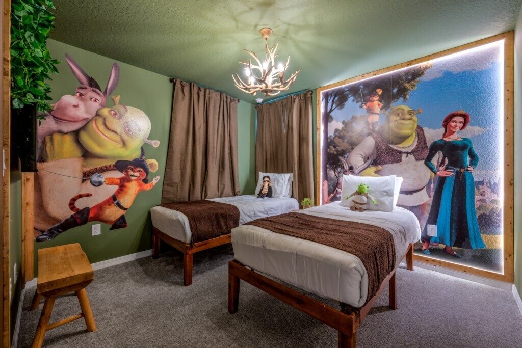 Habitación de hotel con dos camas, un candelabro, un mural de personajes animados y vistas a un bosque.