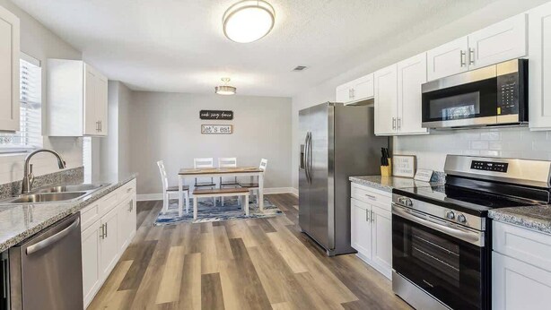 A modern kitchen with white cabinets, stainless steel appliances, and a dining area with a table and chairs. - Beautiful Apartment (Slidell)