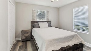 A bedroom with a bed, a nightstand, a ceiling fan, and a window with blinds. - Beautiful Apartment (Slidell)