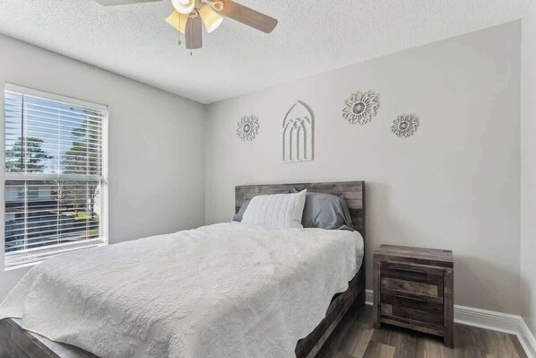 A bedroom with a bed, a nightstand, a ceiling fan, and decorative wall art. - Beautiful Apartment (Slidell)