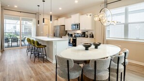 A modern kitchen with white cabinets, a central island, and a dining area with round table and chairs. - New beautiful 5 BEDS~Private Pool (Clermont)