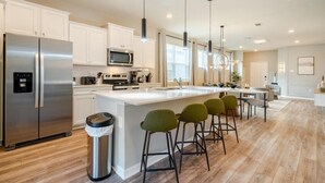 A modern kitchen with white cabinets, stainless steel appliances, and a central island with bar stools. - New beautiful 5 BEDS~Private Pool (Clermont)