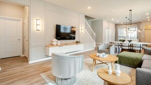 A modern living room with a flat-screen TV, a grey sofa, a round coffee table, and a staircase leading to another level. - New beautiful 5 BEDS~Private Pool (Clermont)