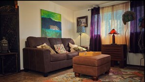 A living room with a brown leather sofa, a wooden side table, a lamp, and a painting on the wall. - Charming bungalow with an Amazing view of Sequoia National Park in Three Rivers. (Three Rivers)