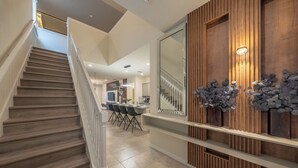 A modern interior with a wooden staircase, a dining area, and a wall-mounted mirror. - Luxe Retreat - Beautiful Modern 7 Bedrooms Home (Davenport)