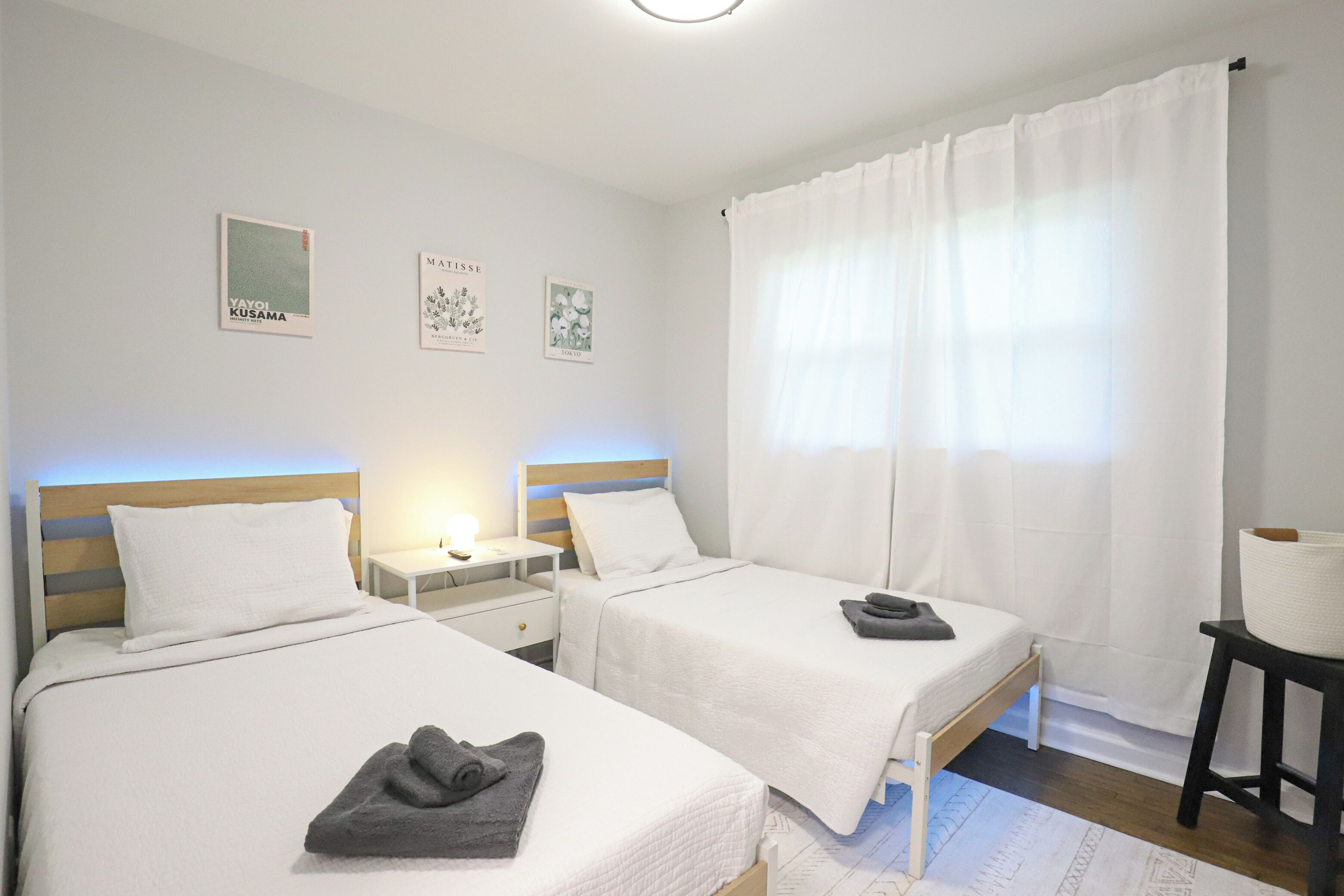 Een slaapkamer met twee bedden, een nachtkastje, een lamp en een raam met gordijnen.