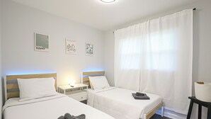 Un dormitorio con dos camas, una mesita de noche, una lámpara y una ventana con cortinas.