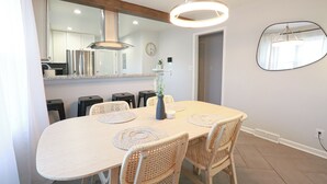 Un comedor con una mesa redonda, sillas de mimbre, un jarrón con flores y una lámpara colgante moderna.