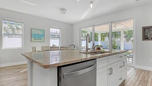 Una cucina moderna con una grande isola, mobili bianchi e vista su un giardino con palme.