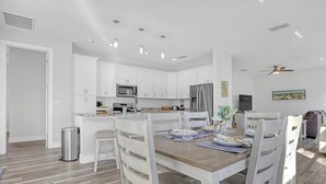 Cucina moderna con mobili bianchi, frigorifero in acciaio inossidabile e zona pranzo con tavolo in legno e sedie bianche.