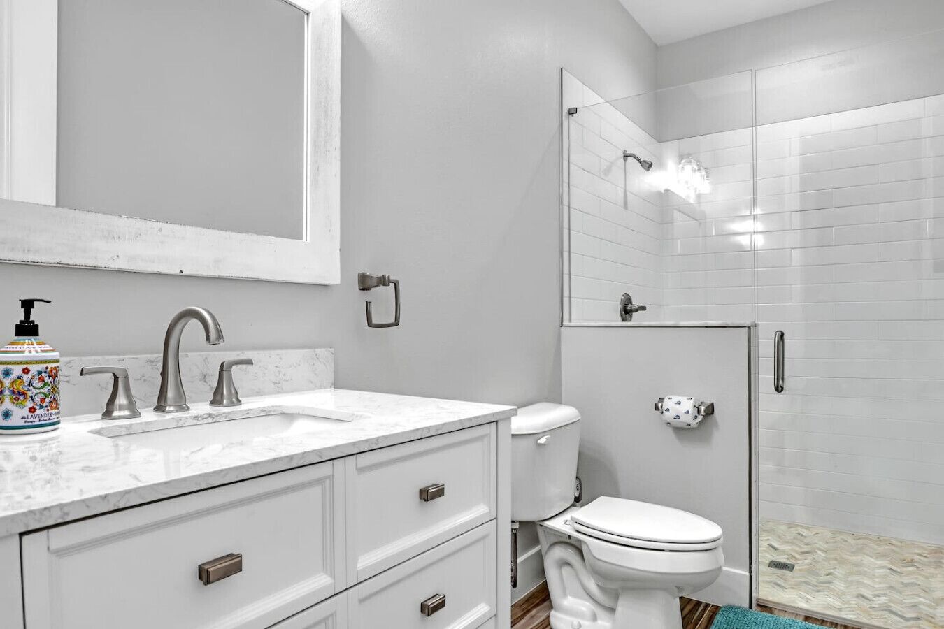 Un baño con un lavamanos blanco, dos grifos, un inodoro y una cabina de ducha de vidrio.
