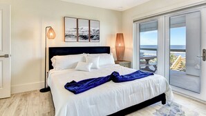 A bedroom with a bed, a ceiling fan, a view of the ocean through a sliding glass door, and a beach scene on the wall. - The White House on Flagler Beach - Unit 23 (Flagler Beach)