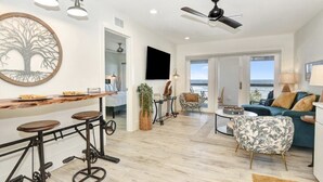 A modern living room with a wooden bar, a ceiling fan, and a view of the ocean. - The White House on Flagler Beach - Unit 22 (Flagler Beach)