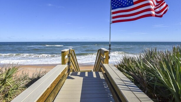 En træpromenade, der fører til en strand med et amerikansk flag.