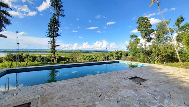 A swimming pool with stone flooring, surrounded by trees and a view of a distant landscape. - Mini Pantanal Paulista with a paradisiacal view, a place to listen to the birds (Ibitiruna)