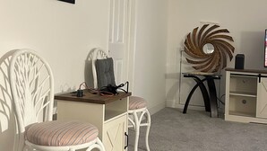 Et værelse med to hvide fletstole, et lille skrivebord med stol, et dekorativt spejl og en spiralformet vægdekoration.