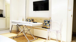 Una habitación moderna con sofá, una mesita, una silla de plástico transparente y un televisor de pantalla plana montado en la pared.