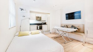 Habitación de hotel moderna con cama, escritorio, sofá y una zona de cocina al fondo.