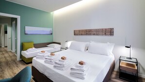 Et hotelværelse med to senge, en grøn lænestol, et natbord med lampe og et billede på væggen.