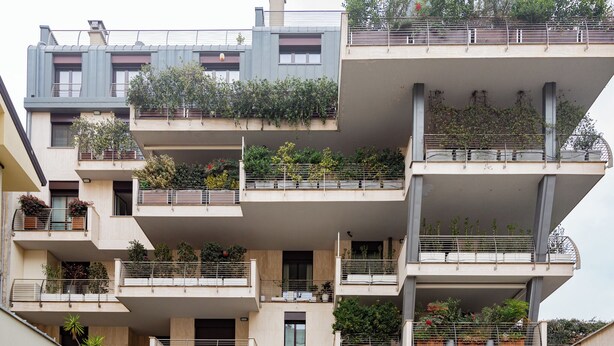 Un immeuble résidentiel à plusieurs étages, doté de balcons, dont certains sont ornés de plantes.