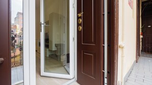 A hotel entrance with a glass door, a brown door with a brass handle, and a tiled walkway leading to a balcony. - Termopili29 Cozy apartment in NoLo by Hospity (Milano)